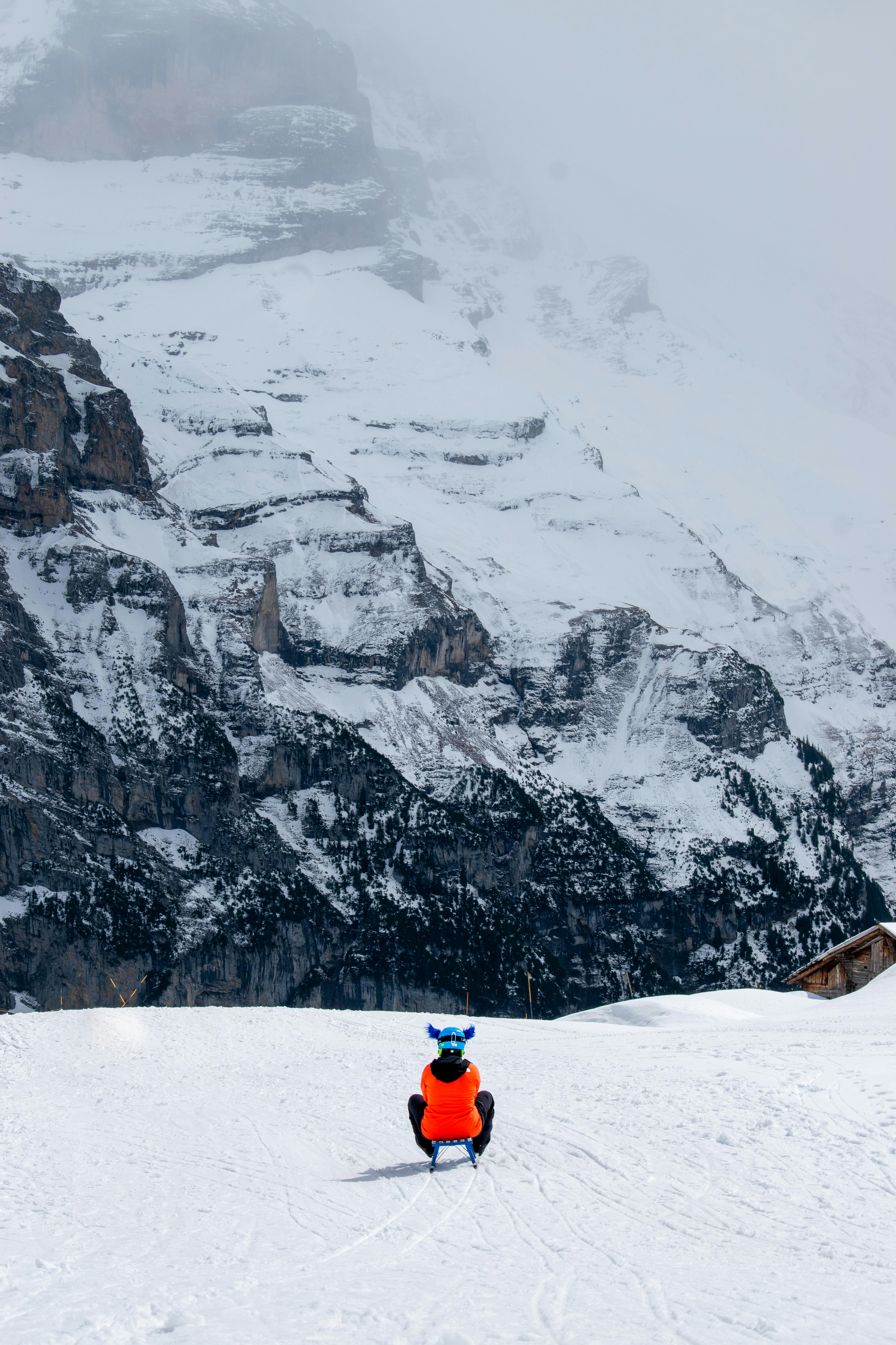 Prescription Goggle Inserts - Person sleds down snowy mountain with dramatic rocky backdrop on a winter day.