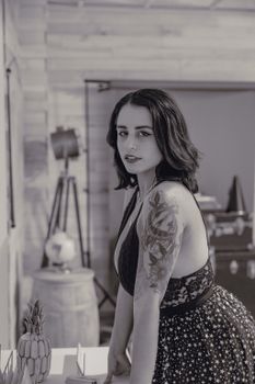 Monochrome portrait of a woman with tattoos, wearing a stylish dress indoors.