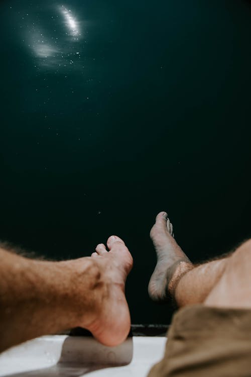 Photo of Bare Feet Dangling Above Body of Water
