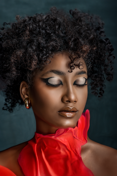 Studio portrait of a woman with curly hair and eyes closed, wearing red, on a gray background.