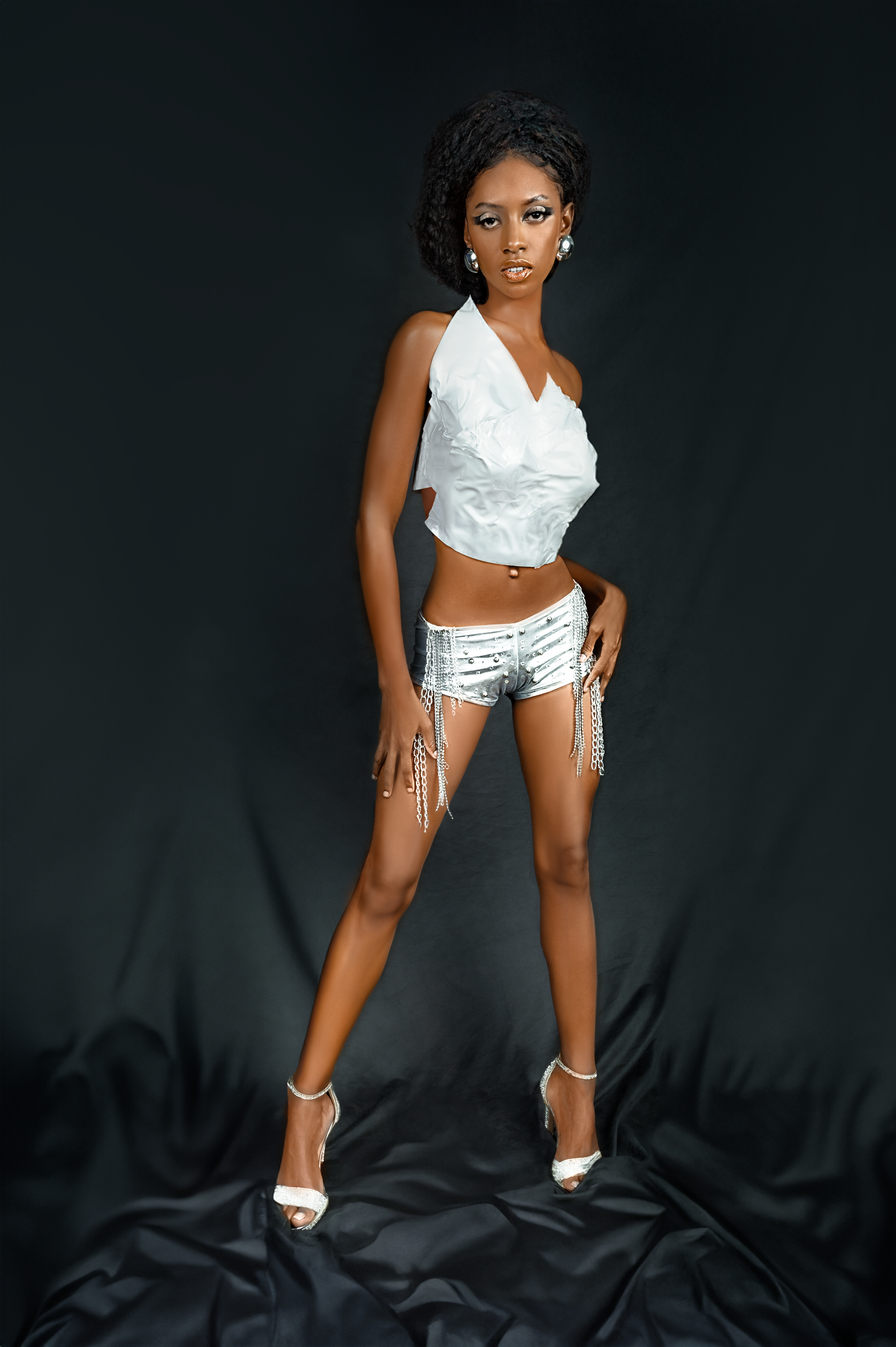 Stylish black woman posing in a studio wearing trendy outfit and jewelry.