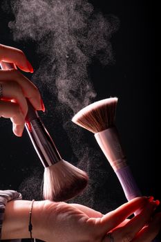 A close-up of makeup brushes displacing powder against a dark background in a studio setting.