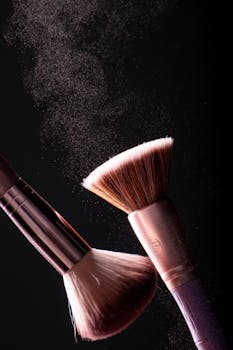 Close-up of makeup brushes with powder on black background, capturing dynamic movement.