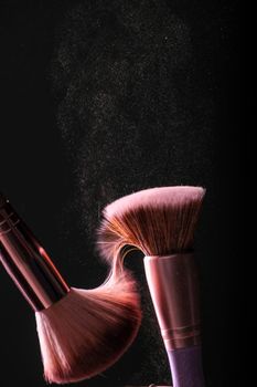 Close-up of makeup brushes in action, creating a cloud of beauty powder against a dark background.