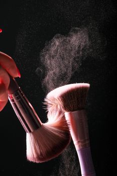 Artistic capture of makeup brushes with a dramatic powder explosion on a black background.
