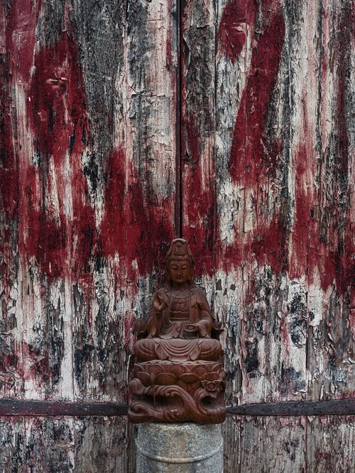 Free A tranquil wooden Buddha figurine sits in front of a rustic, textured wall, evoking a sense of peace and spirituality. Stock Photo