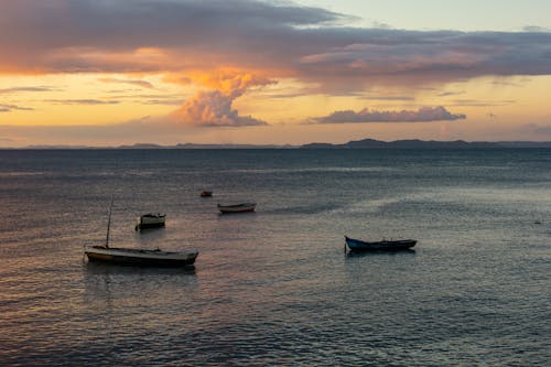 A group of boats in the ocean at sunset