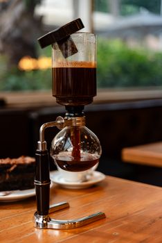 A siphon coffee maker beautifully brewing coffee on a wooden table inside a cozy cafe.