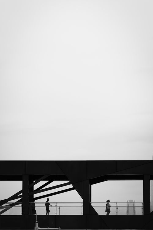 Free Black and white image of silhouettes walking on a modern bridge in an urban setting. Stock Photo