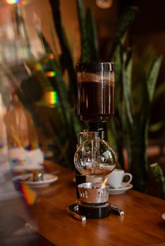A siphon coffee maker elegantly brewing on a wooden table in a cozy indoor setting.