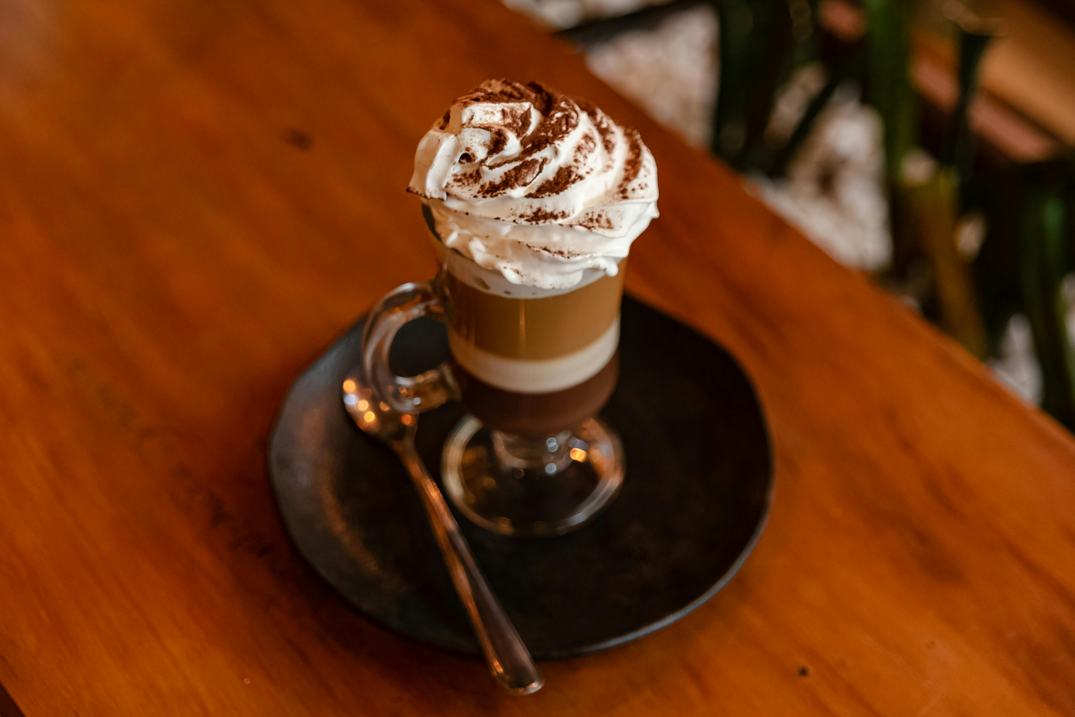 A close-up of a layered coffee topped with whipped cream served on a dark plate.