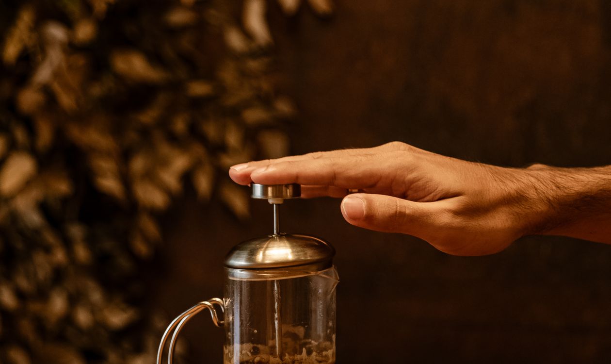 Hand pressing the plunger of a glass French press coffee maker