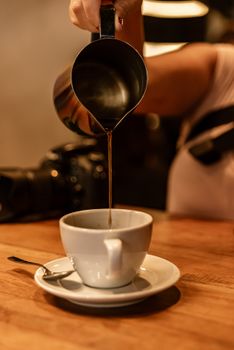 A warm cup of coffee being poured from a stainless steel jug in a cozy cafe atmosphere.
