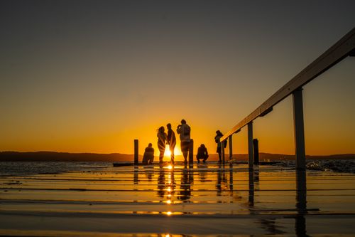 Free Silhouettes of people on a pier against a vibrant sunset over the lake. Stock Photo