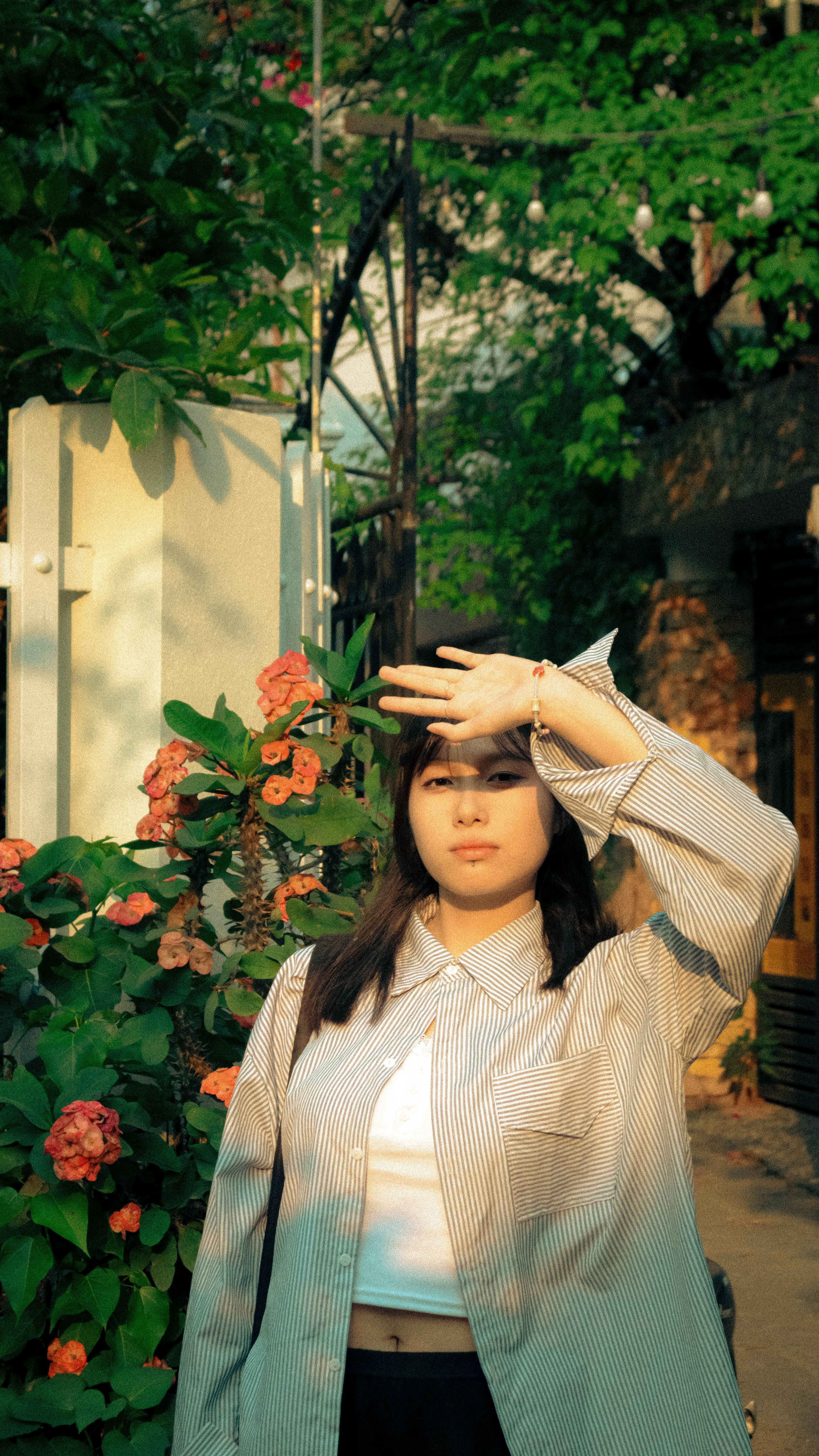 Young woman in a striped shirt posing in a sunny garden with flowers.