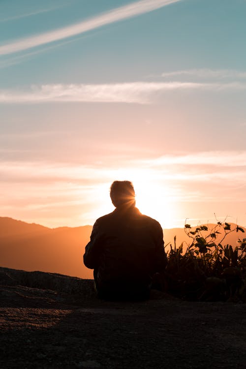 Free Silhouette of Person Sitting and Facing Mountain during Sunset Stock Photo