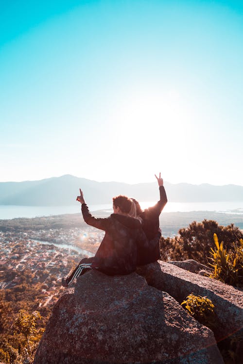 Free Photography of Man and Woman Sitting on Gray Stone While Raising Right and Left Hand Stock Photo