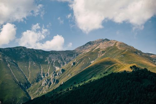 Free A stunning mountain range with vibrant greenery under a bright blue sky and scattered clouds. Stock Photo