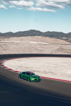 A vibrant green sports car speeds through a mountain track on a clear day.