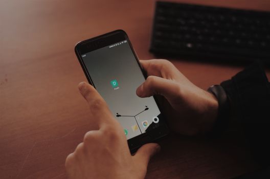 Hands interacting with smartphone on a wooden desk, highlighting modern technology.