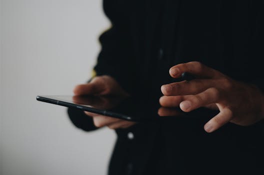 Close-up shot of hands operating a tablet touchscreen in a dark setting.