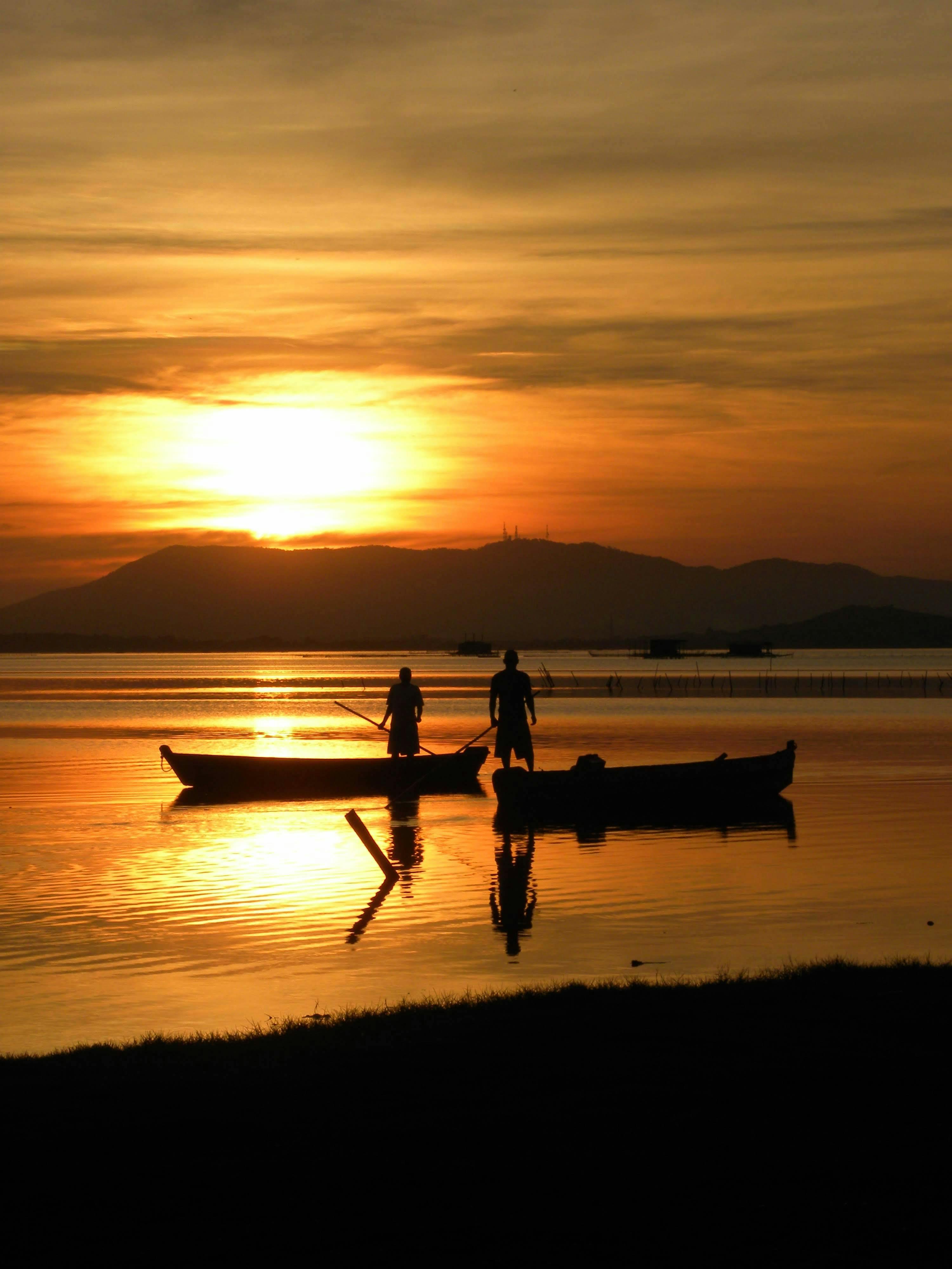日出时分，渔民划船的剪影倒映在宁静的湖面上