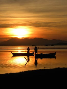日出时分，渔民划船的剪影倒映在宁静的湖面上