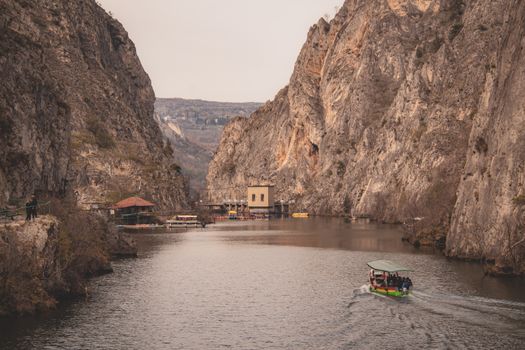 Explore the stunning view of Matka Canyon with a riverboat navigating through rocky cliffs.