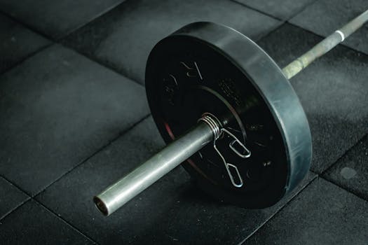 Detailed view of a barbell with heavy weights resting on a dark gym floor mat.