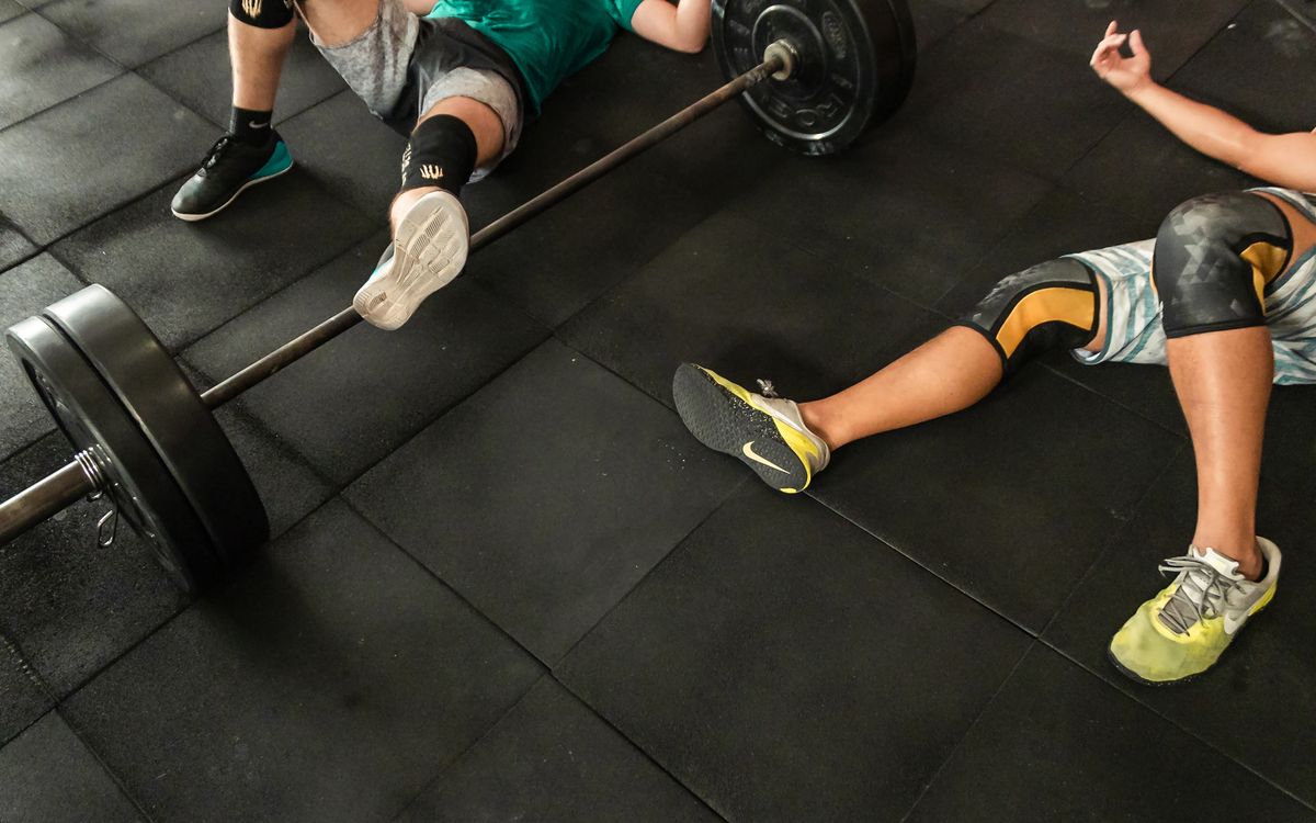 Athletes resting on a gym floor beside heavy barbells after an intense weightlifting session.