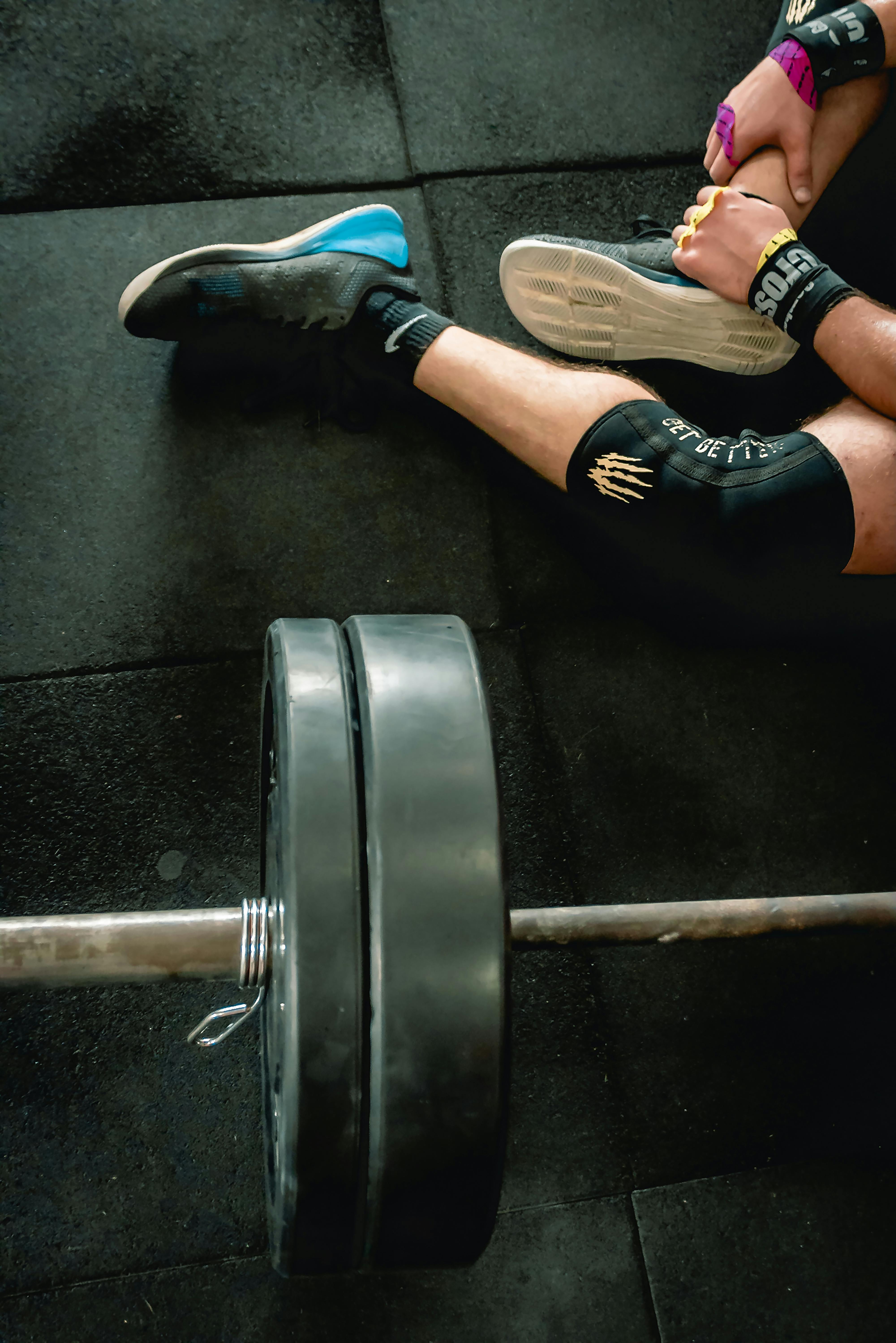 person in black shoes sitting beside barbell