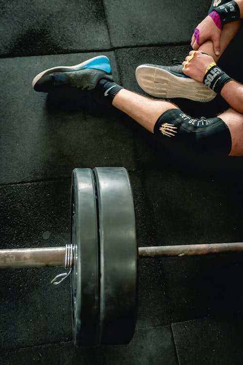 Person in Black Shoes Sitting Beside Barbell