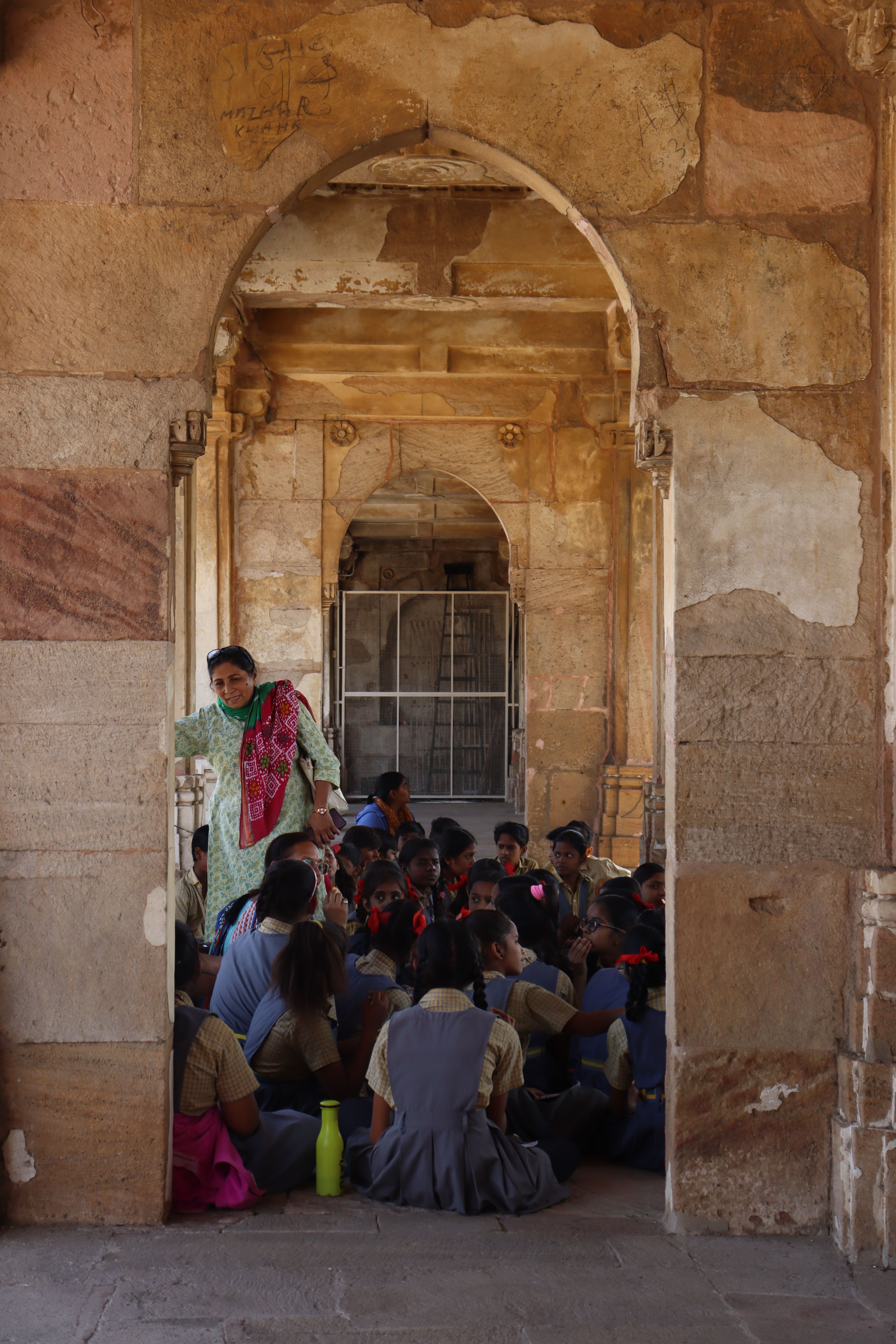 Group of children learning while sitting inside an ancient stone archway with a teacher.