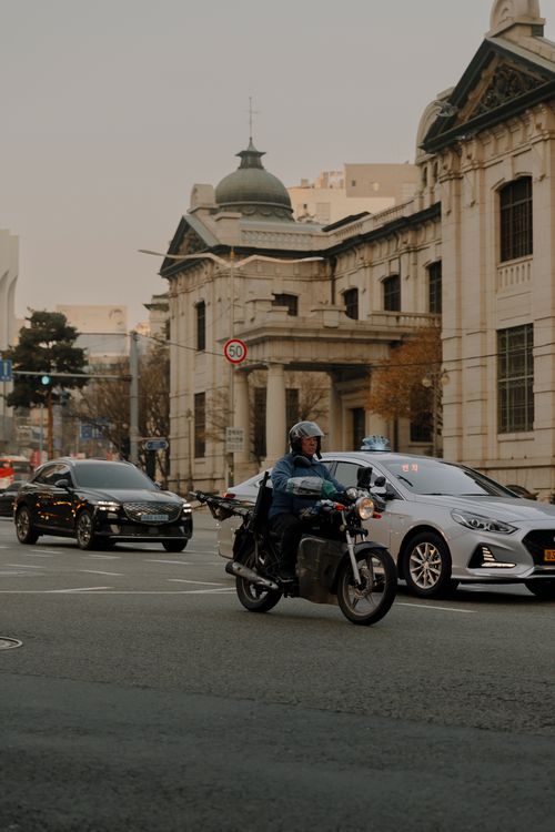 Free A motorcyclist rides in busy city traffic with historic buildings in the background. Stock Photo