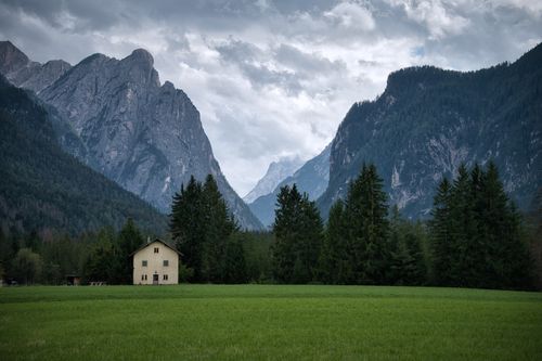 Free Lush green valley in Toblach with a solitary house and majestic mountains under an overcast sky. Stock Photo