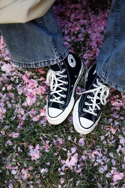Top view of casual jeans and black sneakers on grass covered with pink blossom petals.