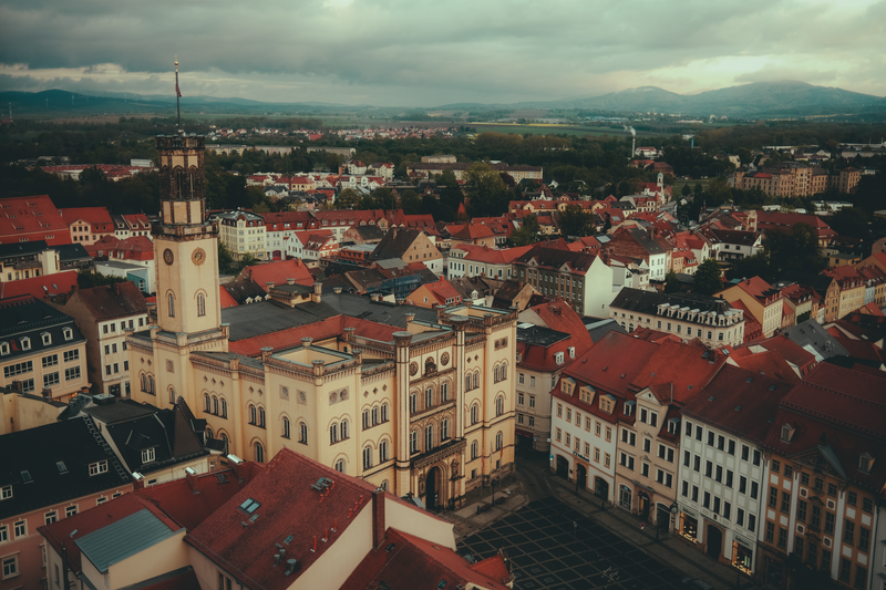 Drone shot of Zittau Town Hall surrounded by red-roofed buildings under cloudy skies.