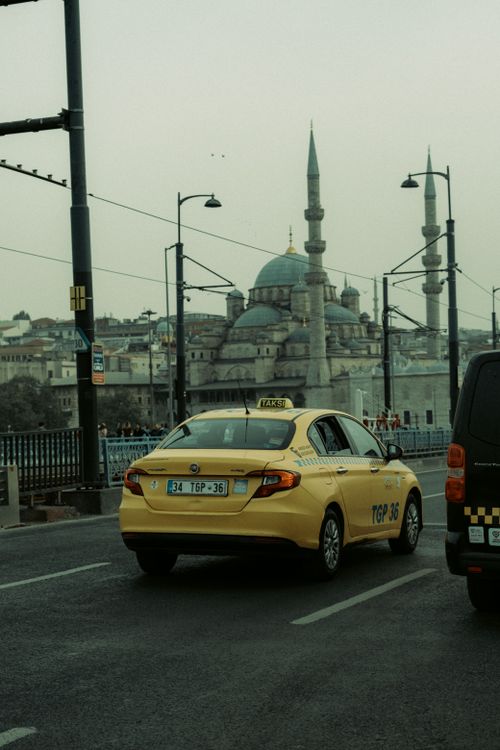 Free Yellow taxi driving in front of the iconic New Mosque in Istanbul, Türkiye on a city street. Stock Photo