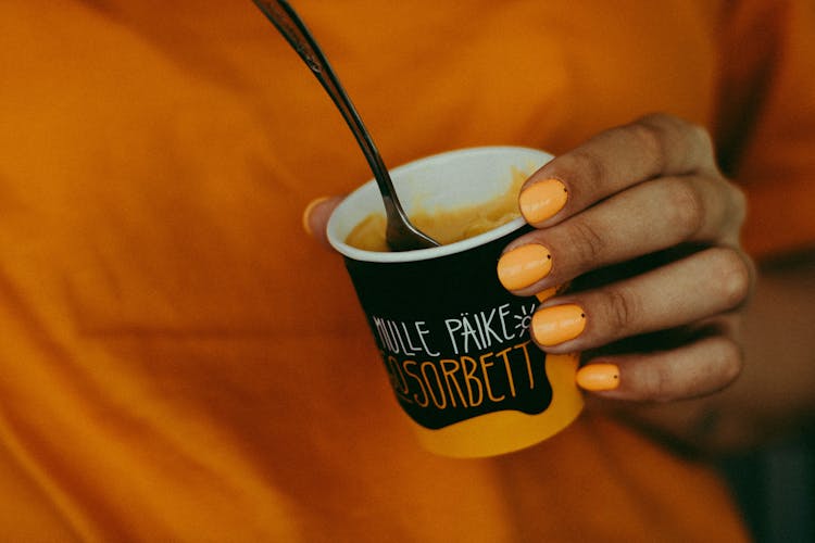 Close-up Photo Of A Woman Holding A Cup Of Mango Flavored Sorbet Ice Cream