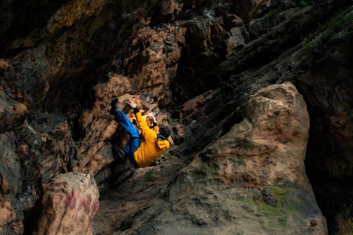 A person in a yellow jacket climbing up a rock