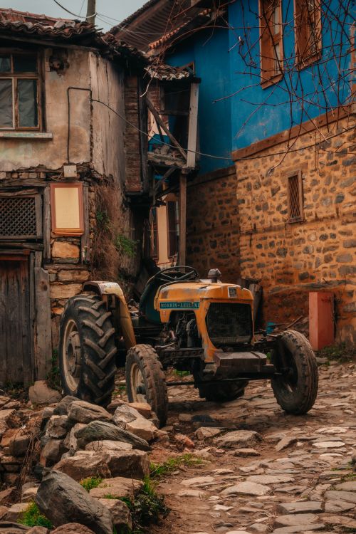 Free An old tractor parked on a stone path between rustic village houses. Stock Photo