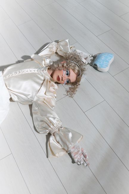 Fashion model in a white dress lying on a minimalist floor with a vintage bag.