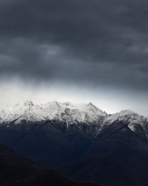 Dramatic snow-covered peaks under cloudy skies in Sochi, Russia.
