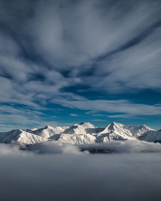 Stunning snow-covered mountain peaks in Sochi, Russia, beneath dramatic clouds and a blue sky.