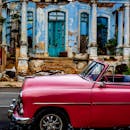 一辆粉红色的经典汽车停在哈瓦那一栋风化的建筑旁，展现出怀旧的城市魅力