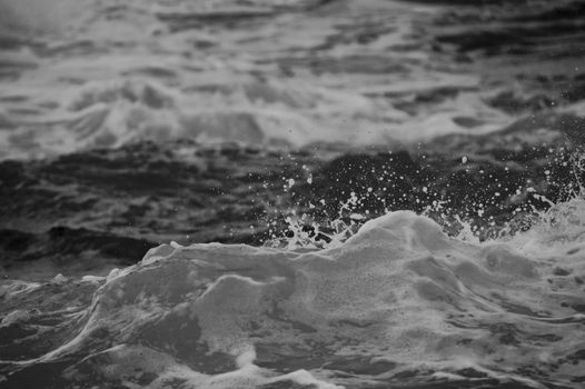 A dramatic black and white photo capturing the splashing waves of the ocean.