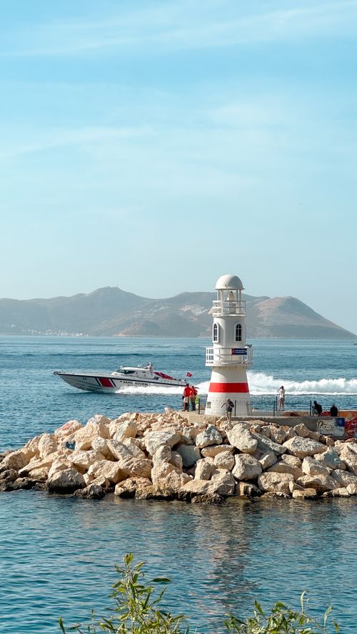 Free Scenic view of a lighthouse with a motorboat passing by on a rocky Turkish seaside. Stock Photo