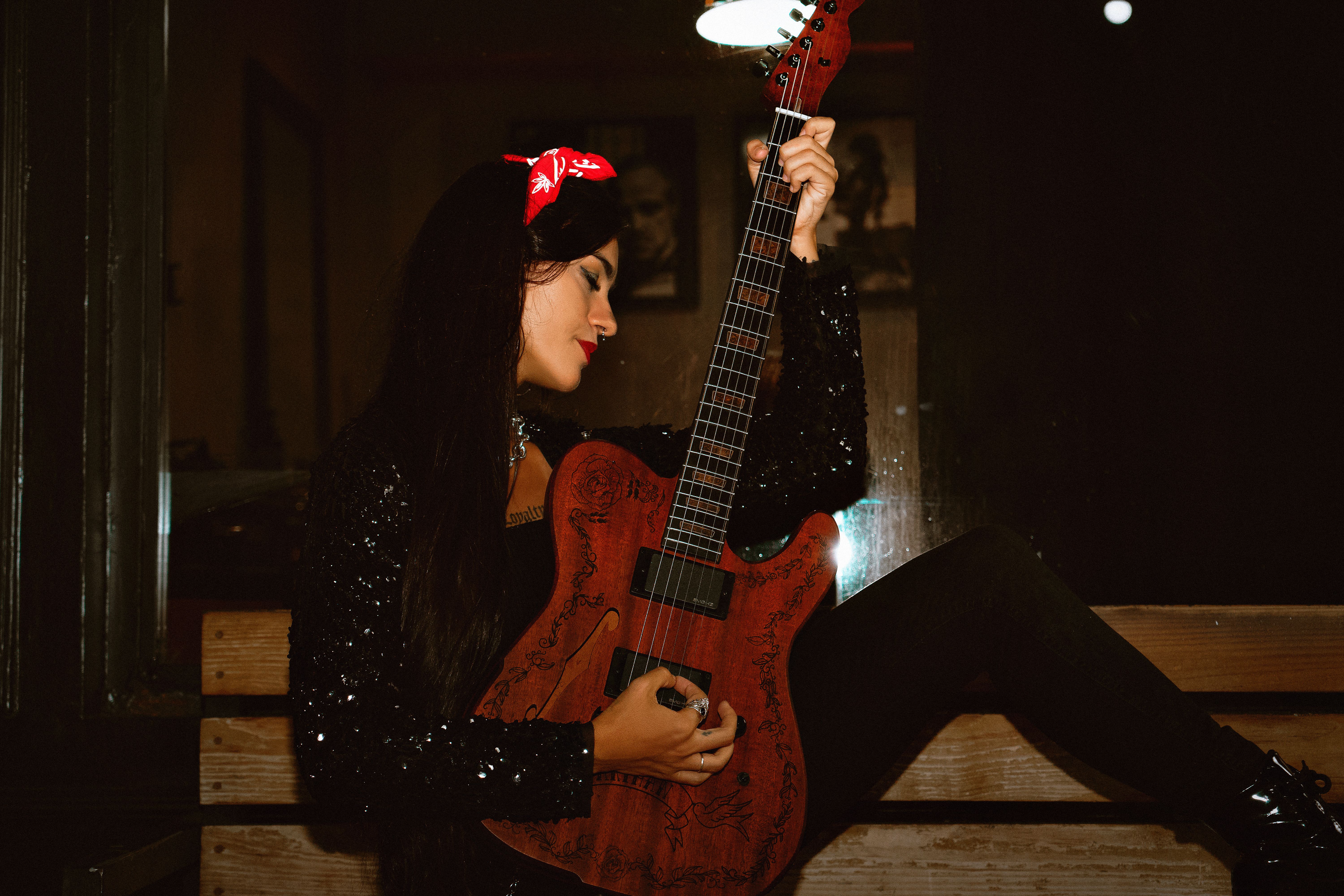 A woman playing an electric guitar indoors, exuding a stylish and moody vibe.