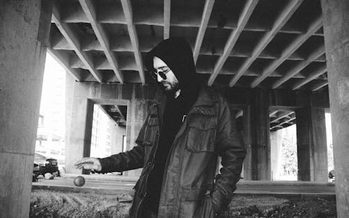 A man in a hoodie and jacket standing under a bridge
