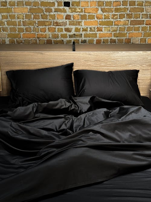 A bed with black sheets and pillows on top of a brick wall